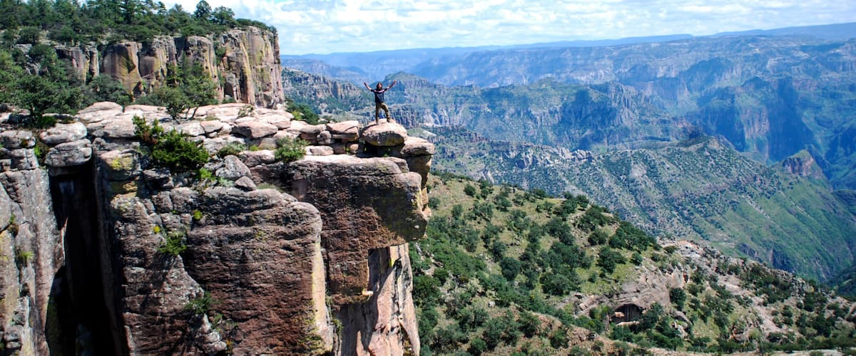 A person standing on a rocky cliff with a vast canyon landscape in the background.