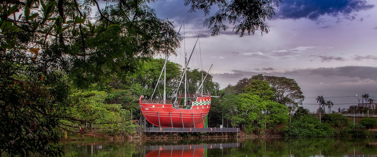 A red boat on a calm lake surrounded by lush greenery and trees.