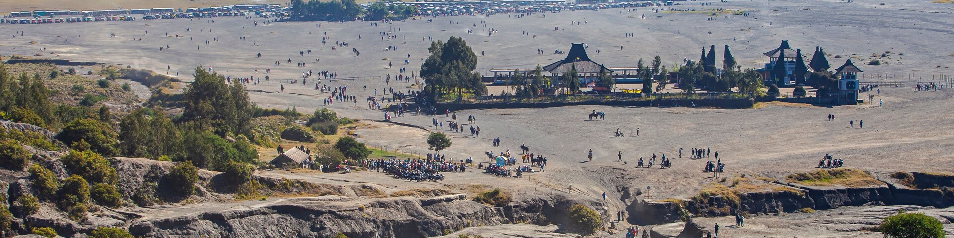 A vast desert landscape with scattered trees and a large building complex in the distance.