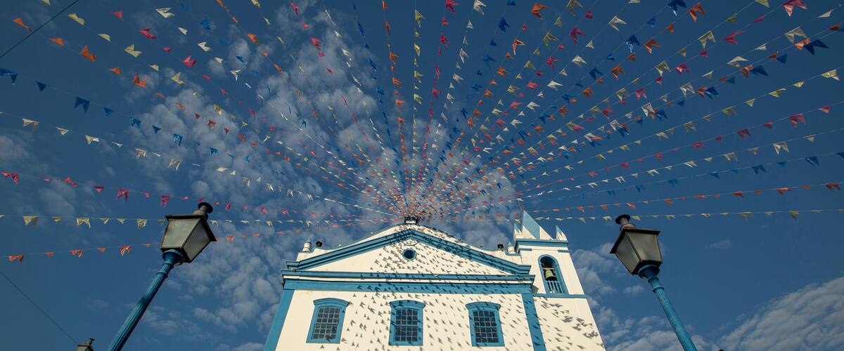 A building with a blue and white facade, surrounded by a string of colorful triangular flags against a blue sky with clouds.