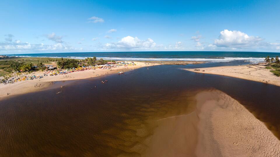 A beach with clear water, a sandy shore, and a distant view of the ocean.