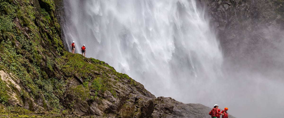 A waterfall cascading down a rocky cliff into a river surrounded by rocks and greenery.