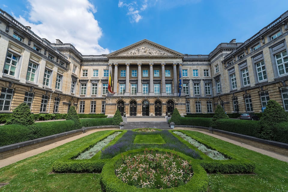 A grand neoclassical building with symmetrical architecture, a central garden, and flags.