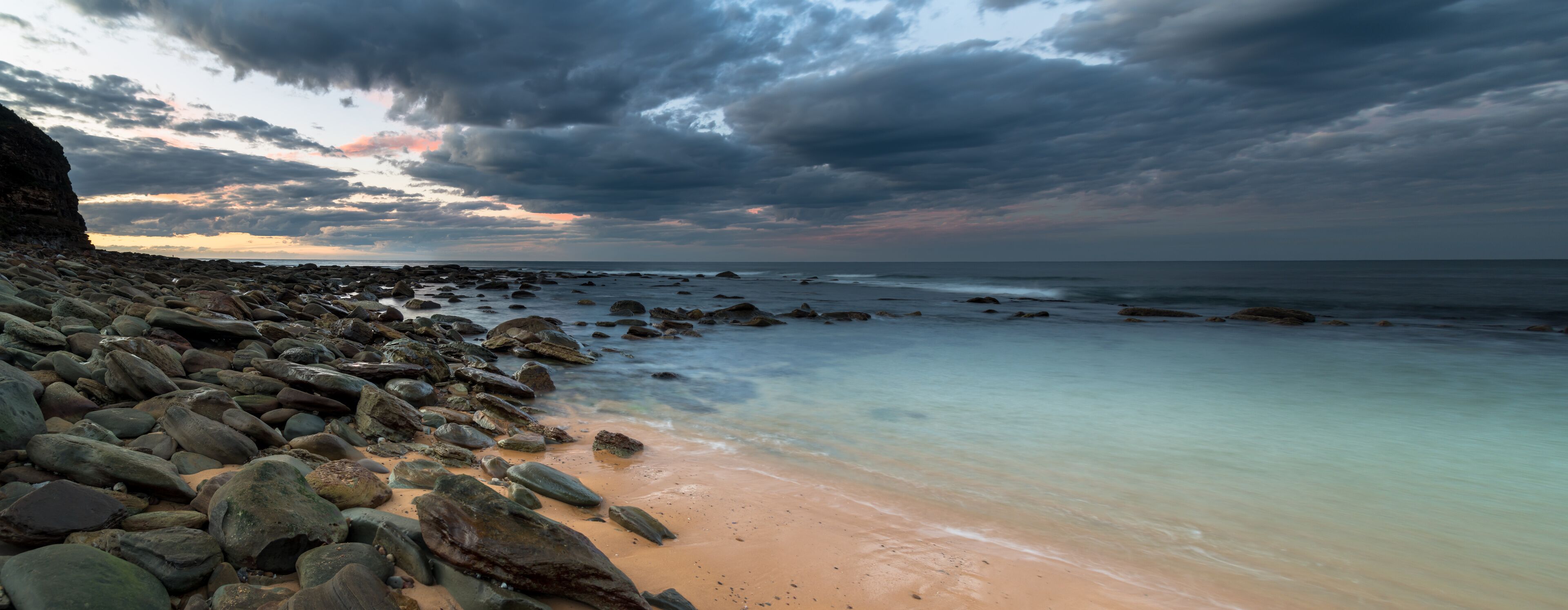 A rocky beach with a calm sea and a cloudy sky.