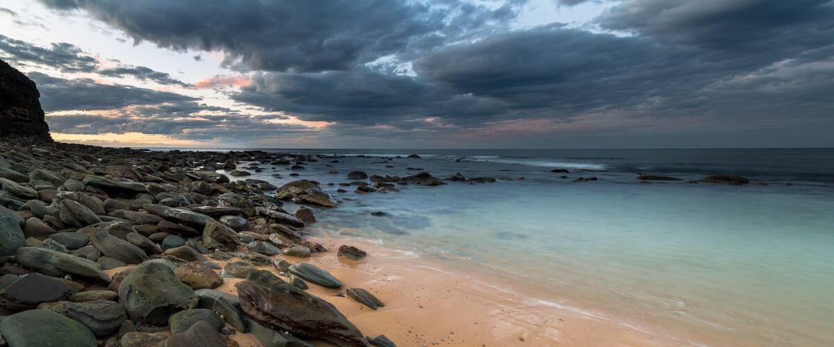 A rocky beach with a calm sea and a cloudy sky.