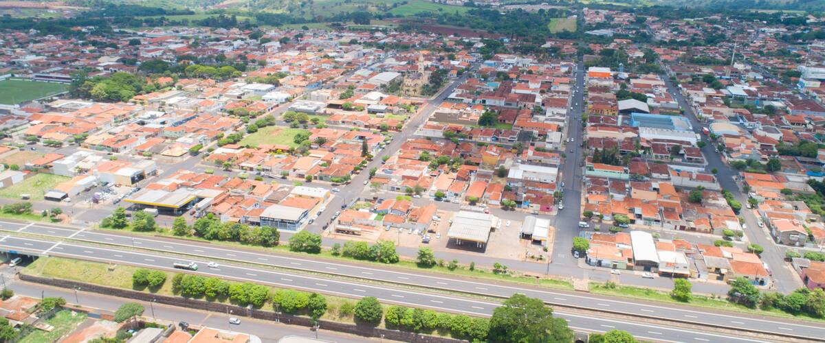 An aerial view of a town with red-roofed buildings, a main road, and surrounding green fields.