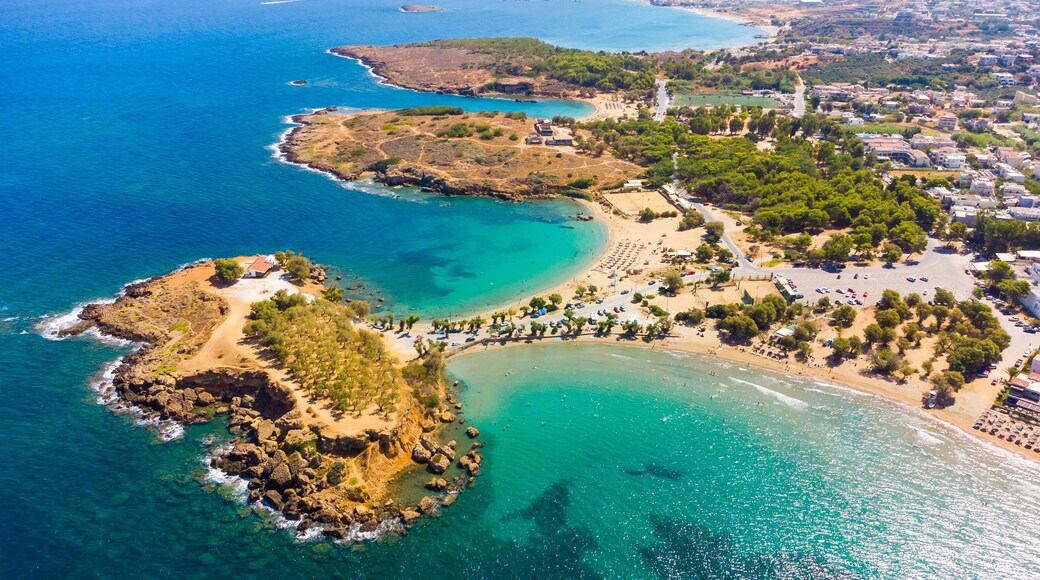 An aerial view of a coastal town with clear blue waters, a sandy beach, and a rocky peninsula.