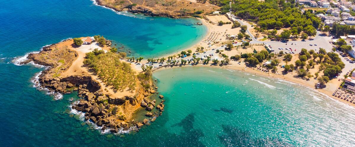 An aerial view of a coastal town with clear blue waters, a sandy beach, and a rocky peninsula.