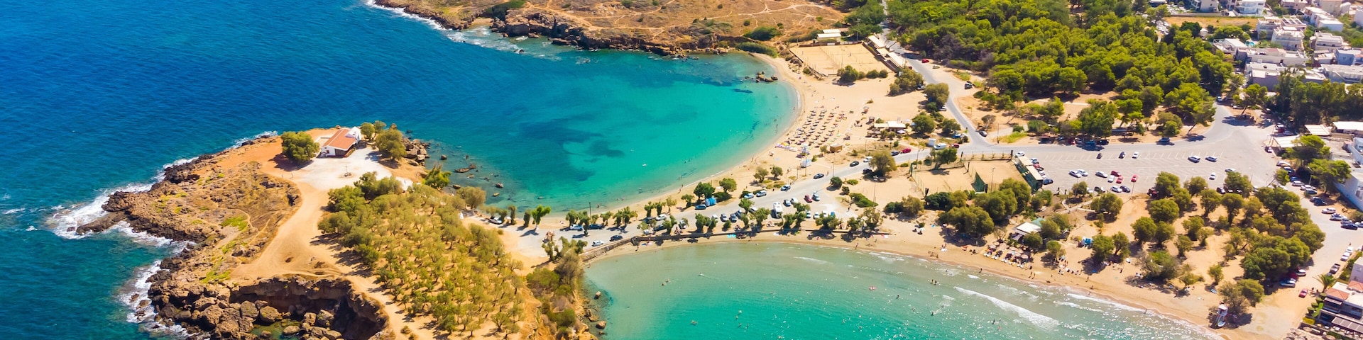 An aerial view of a coastal town with clear blue waters, a sandy beach, and a rocky peninsula.
