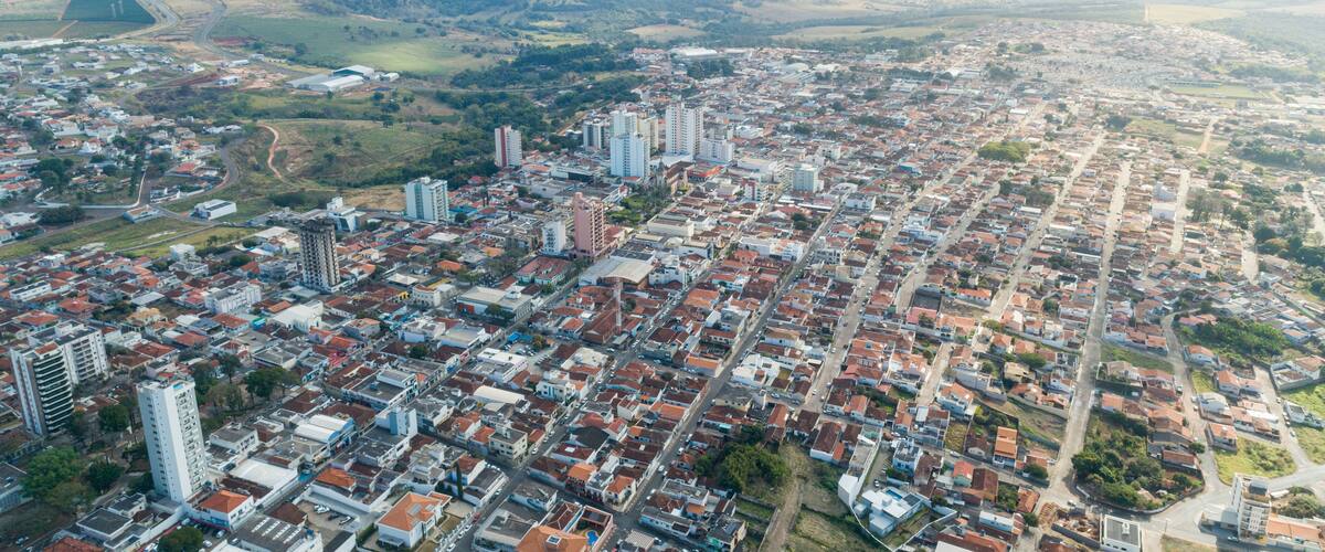 A cityscape with dense urban development, surrounded by green hills and a distant mountain range.