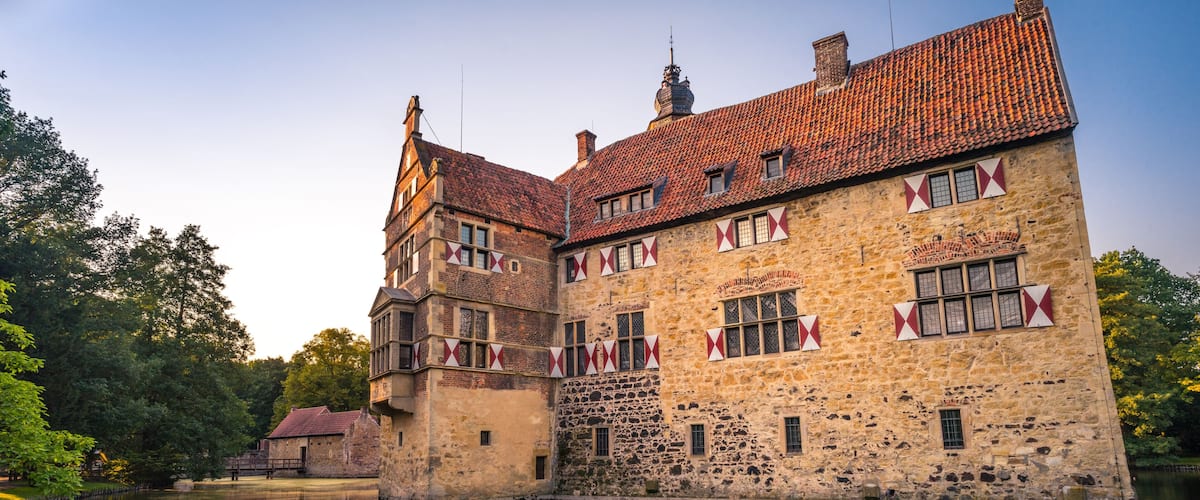 A historic stone building with a red-tiled roof and red and white triangular flags.
