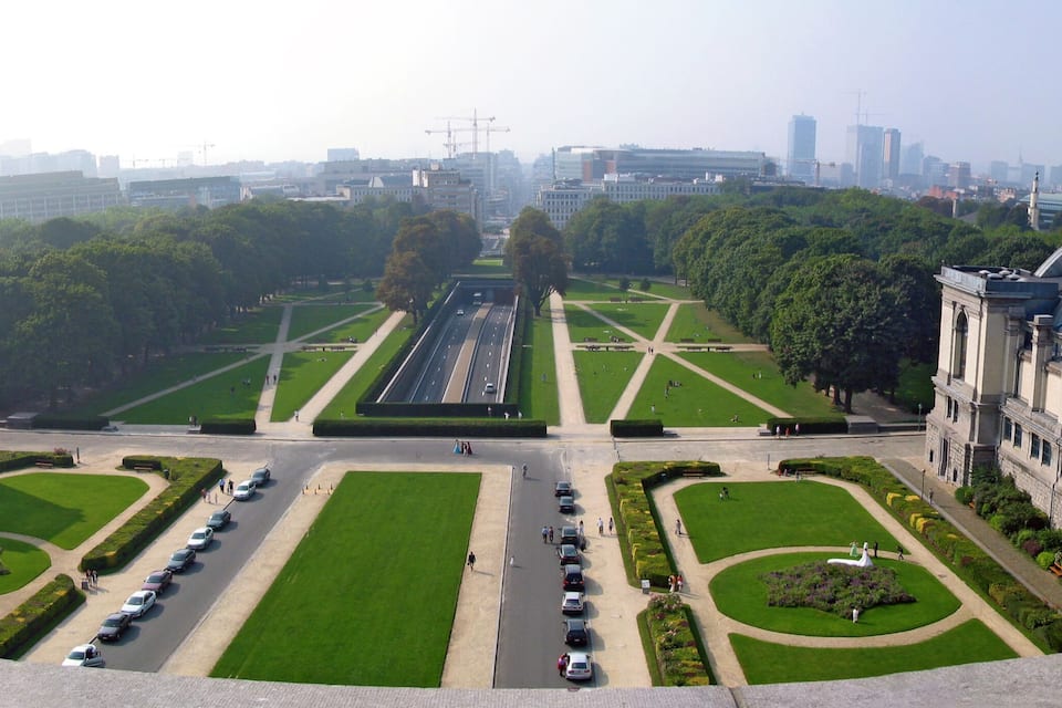 A cityscape with a large green park, a long avenue lined with trees, and a prominent building with a dome.
