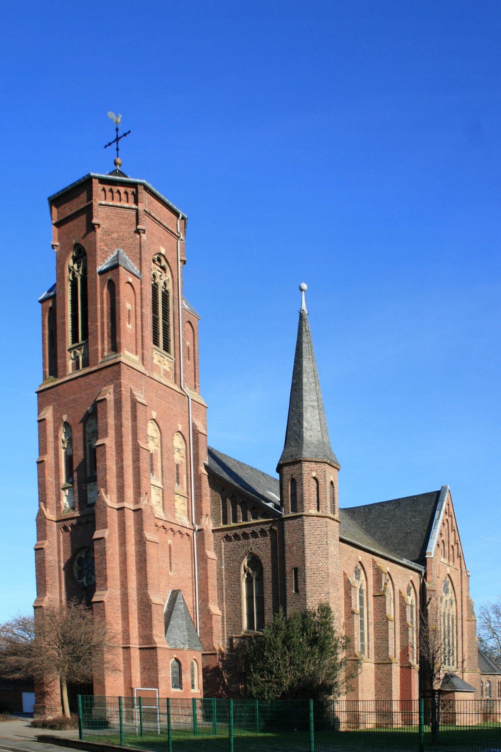 A red brick church with a tall tower and a pointed steeple.