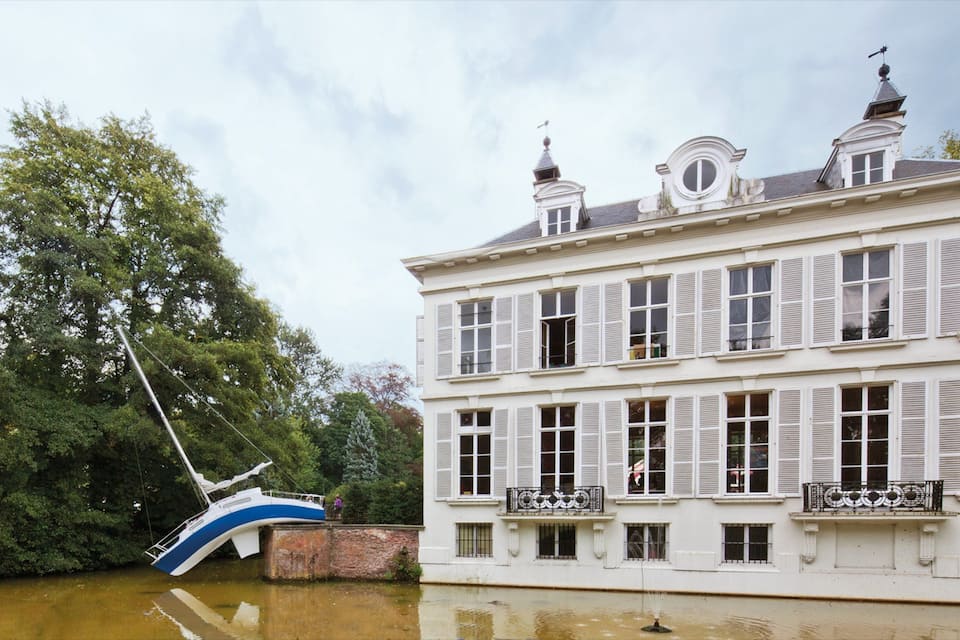 Een wit gebouw met luiken, een brug en een rivier.