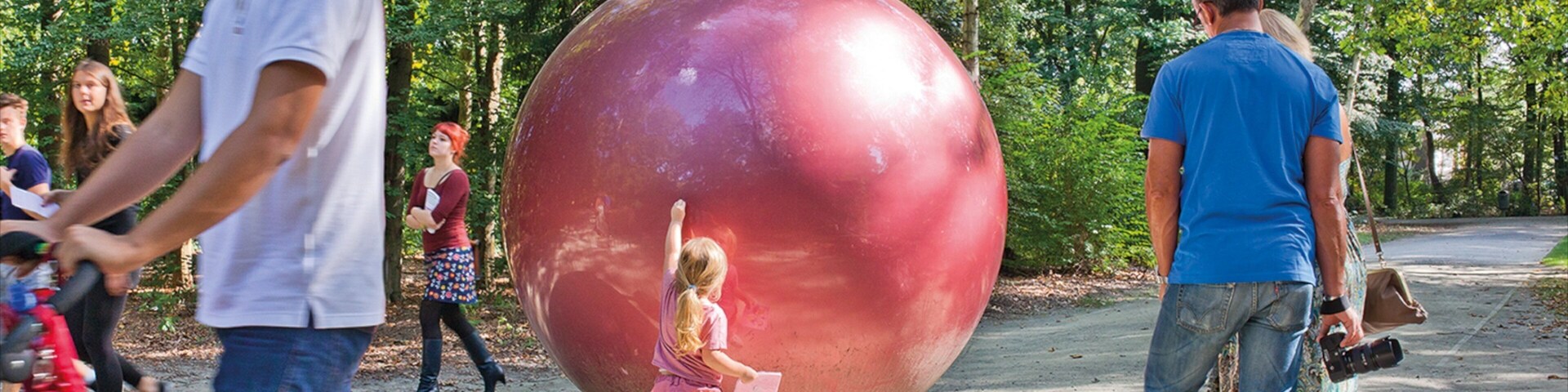 Una esfera roja grande en un parque, con gente alrededor.