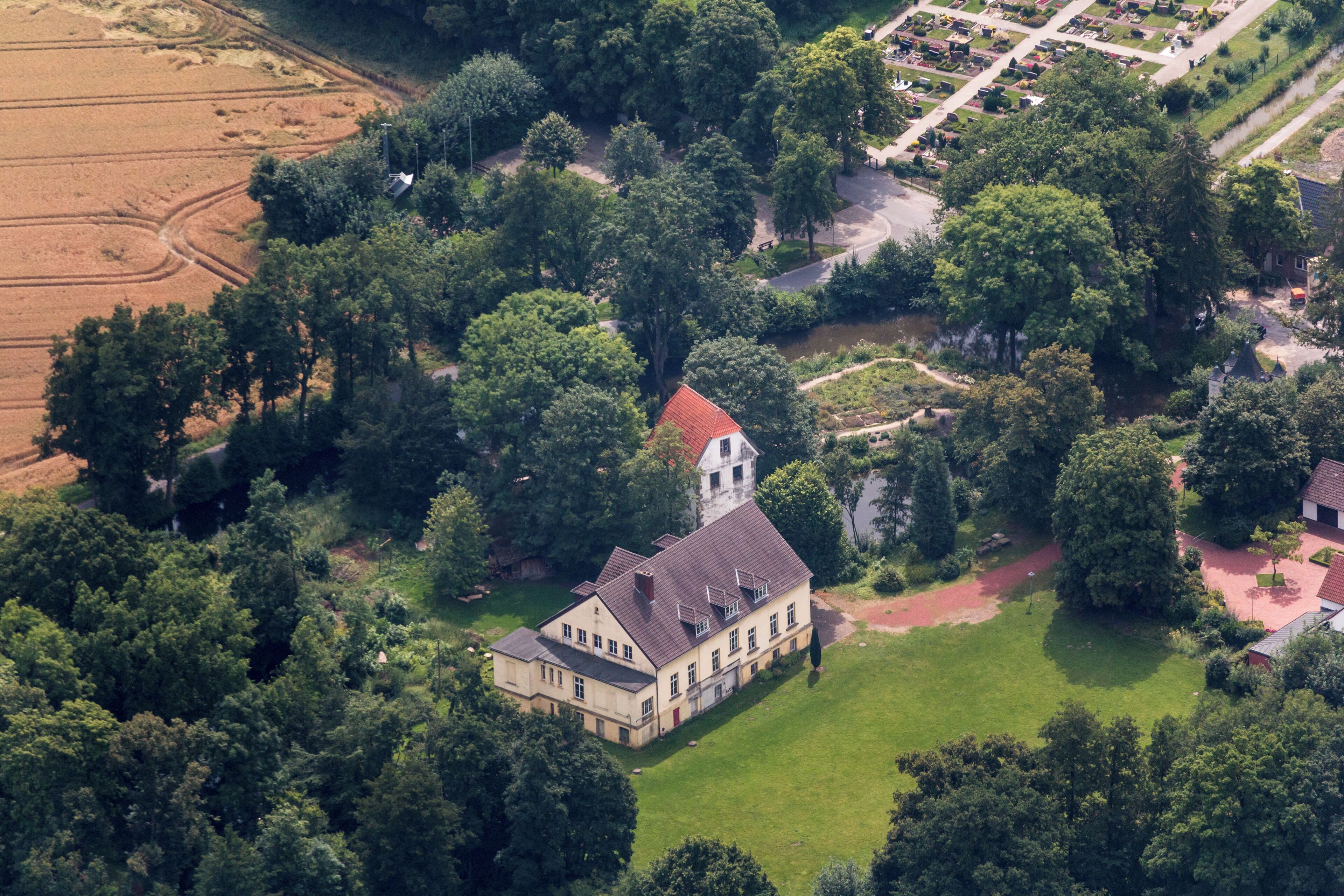 An aerial view of a large estate with a prominent building featuring a red roof, surrounded by lush greenery and a well-maintained garden.
