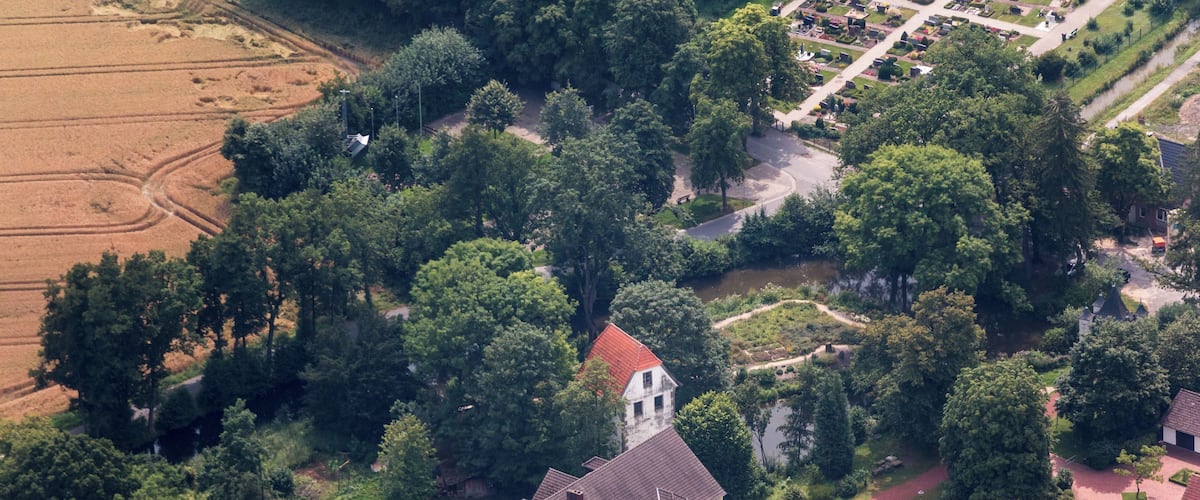An aerial view of a large estate with a prominent building featuring a red roof, surrounded by lush greenery and a well-maintained garden.