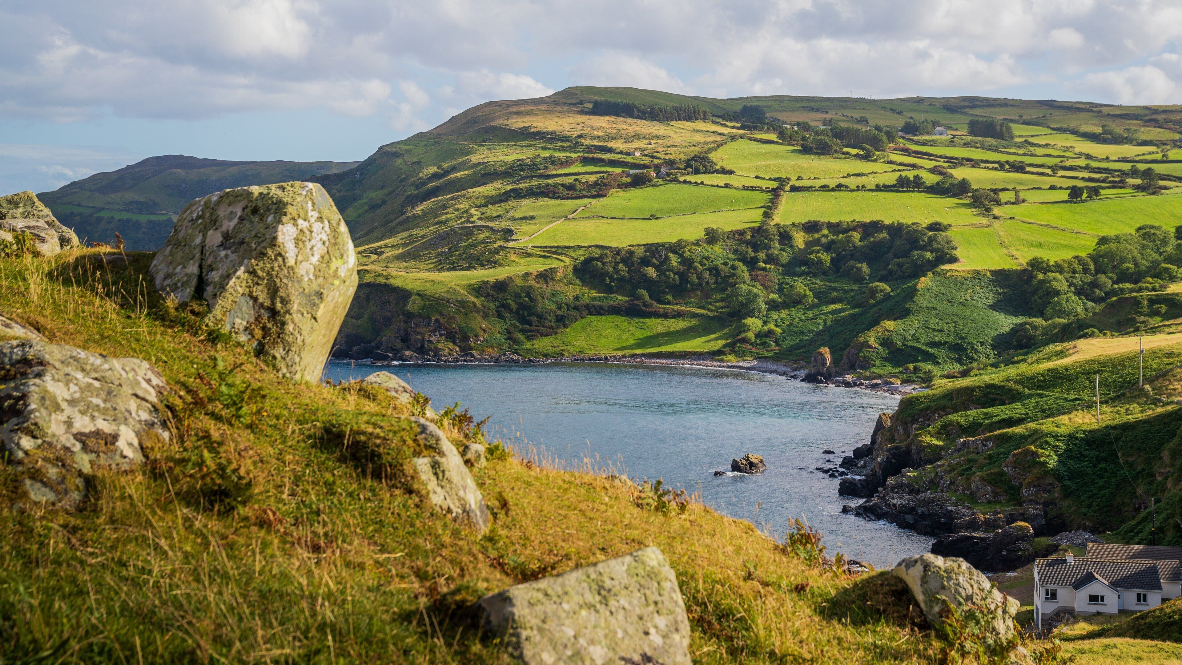 A coastal landscape with rolling hills, a small house, and a rocky shoreline.