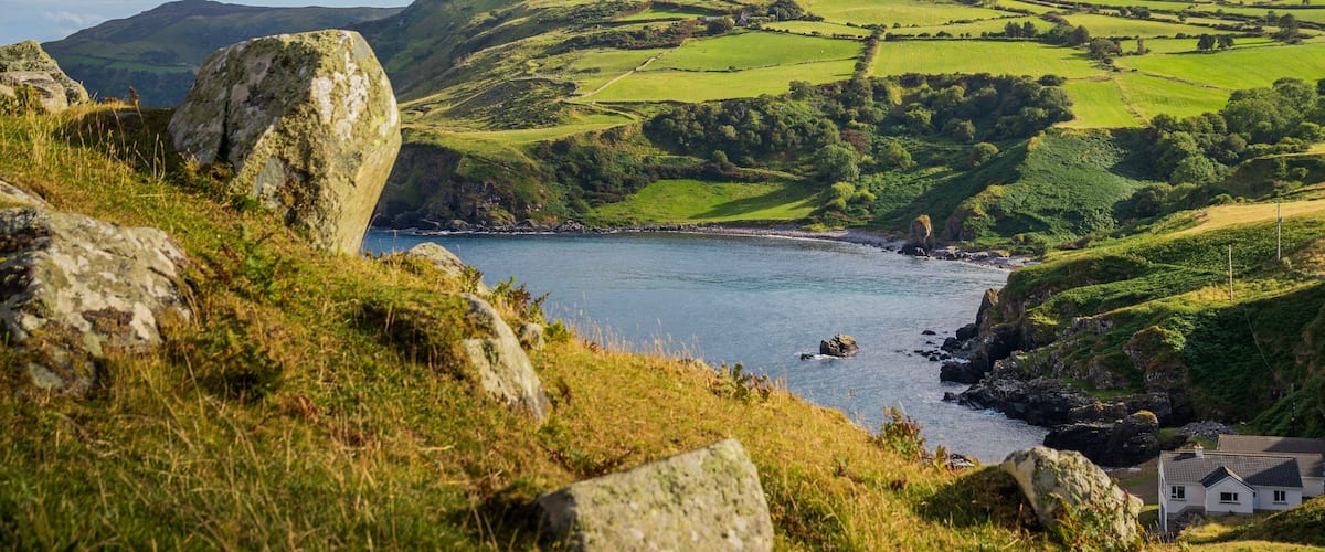 A coastal landscape with rolling hills, a small house, and a rocky shoreline.