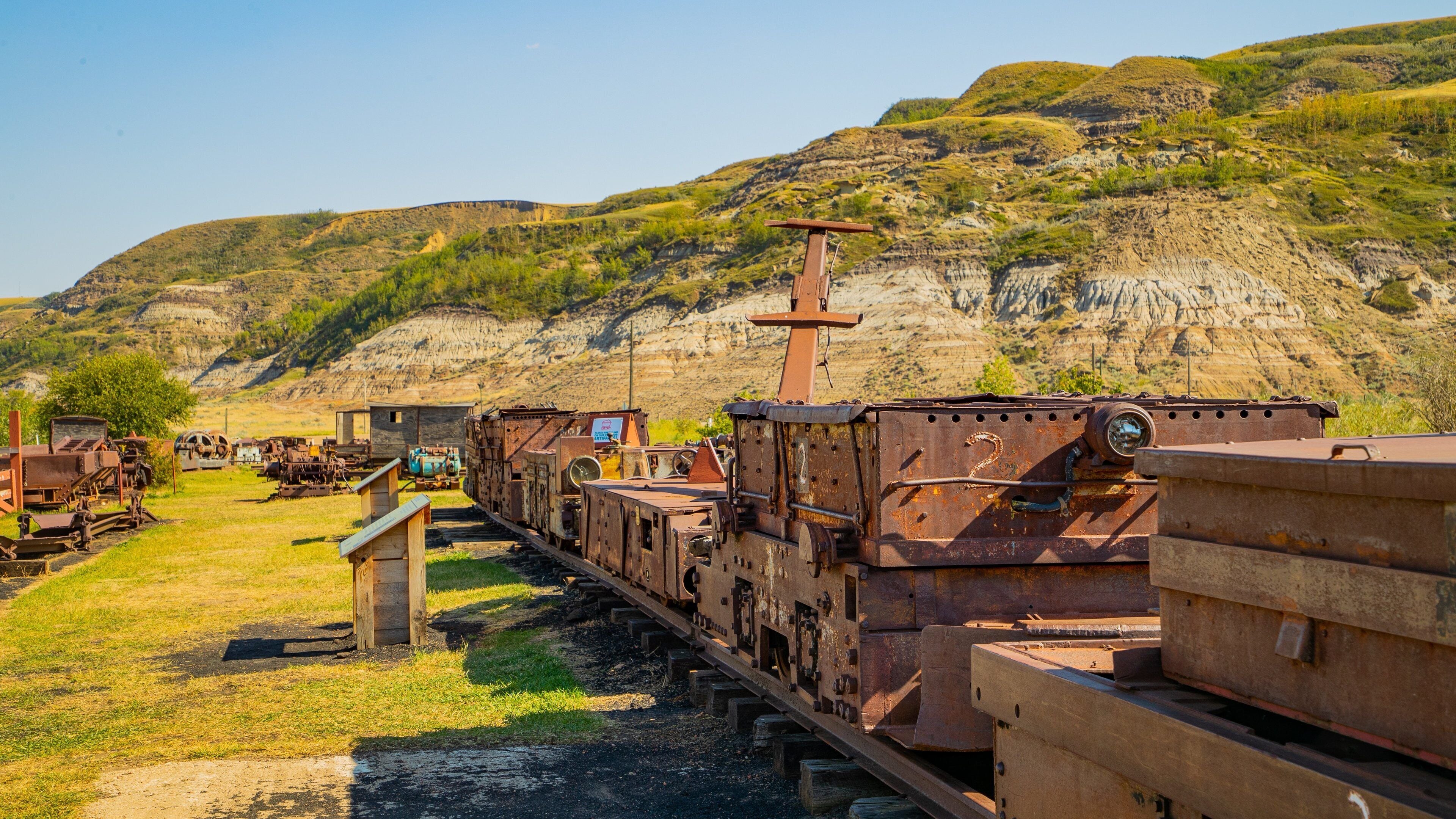 A rusty train on tracks with mountains in the background.