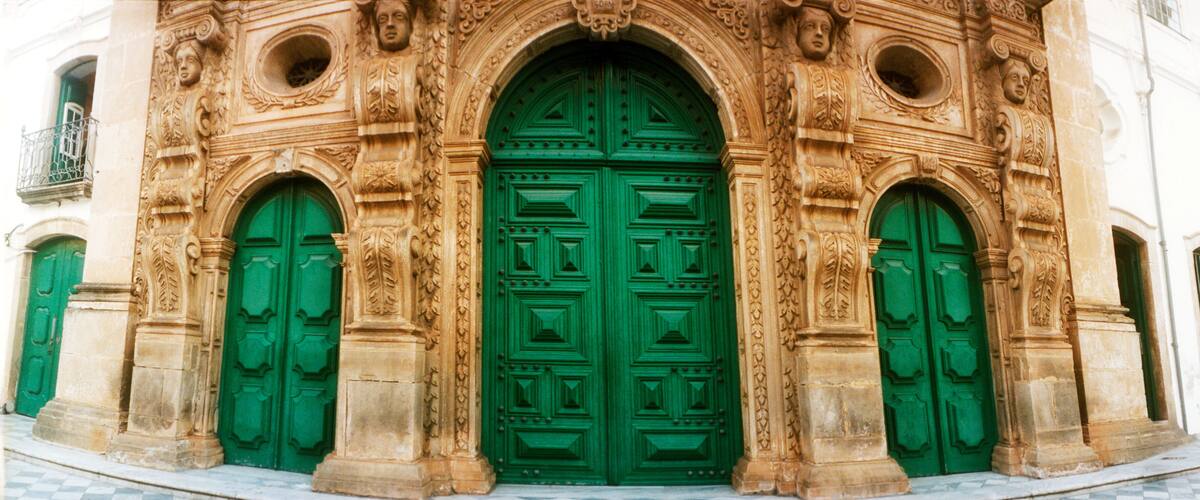 A building with ornate stone carvings and green doors.