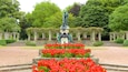 A statue in a garden with red flowers and stone steps.