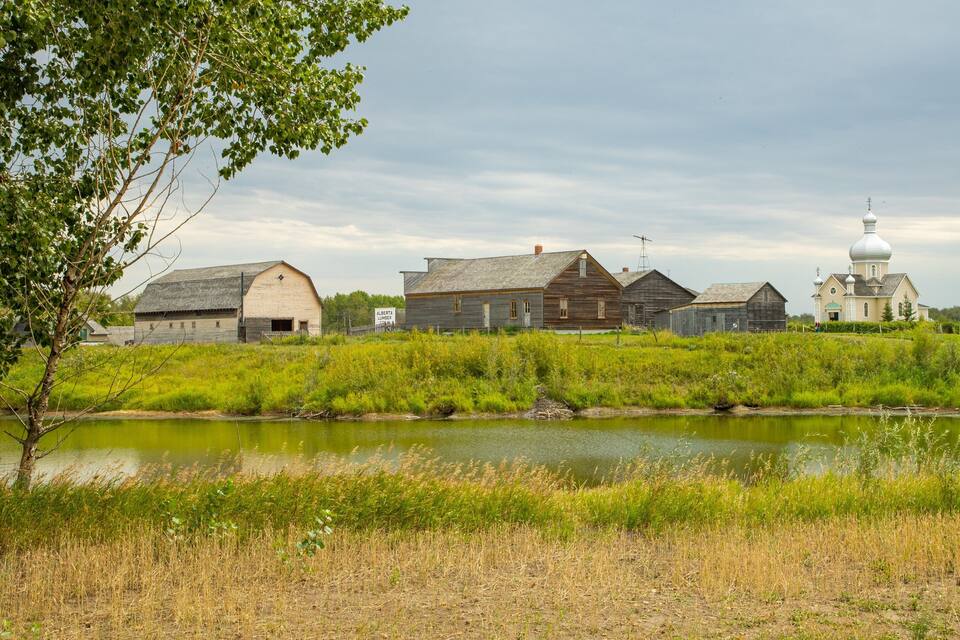 Ländliche Landschaft mit Teich, Holzhäusern und Kirche.