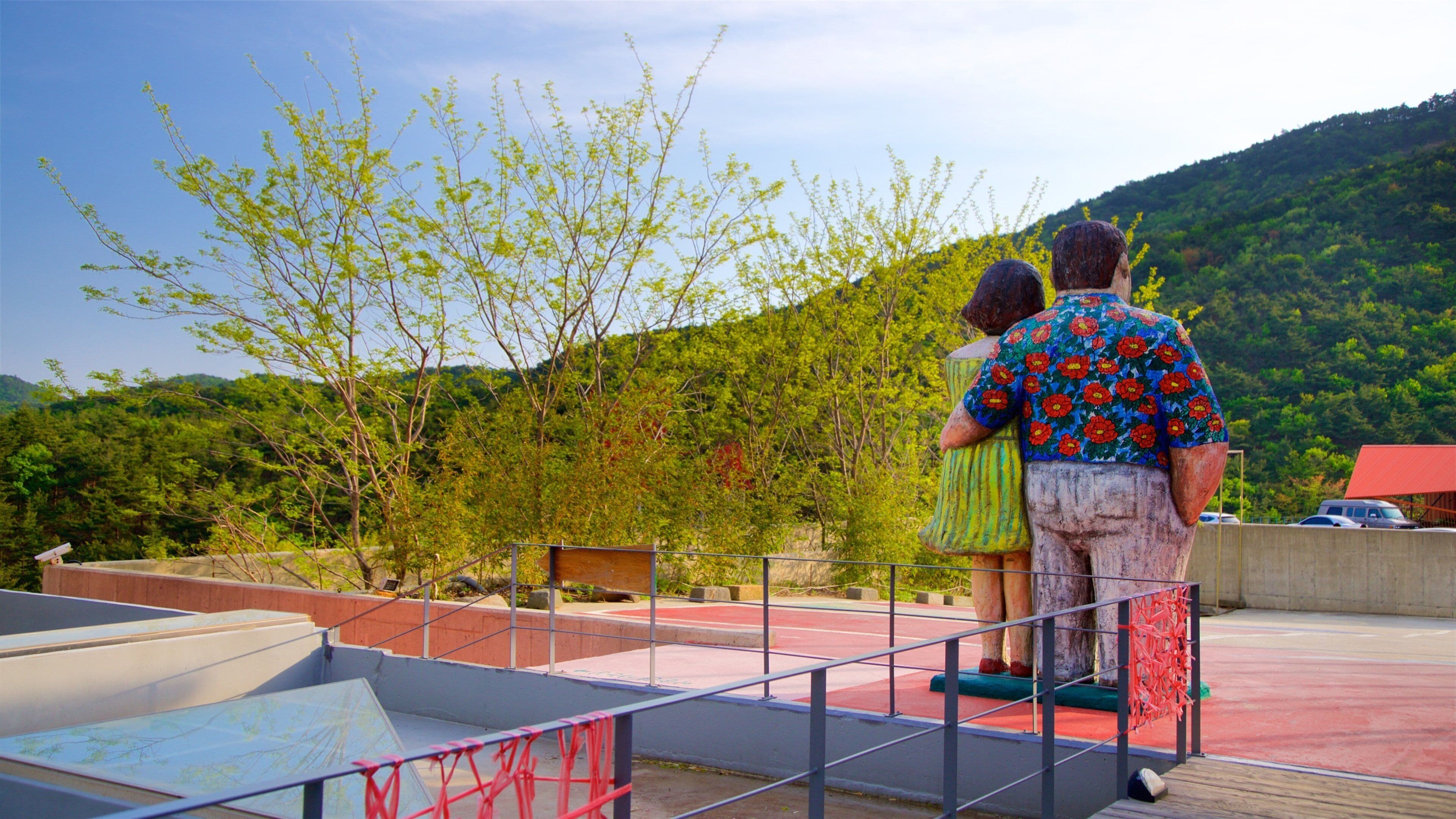 A couple standing on a viewing platform overlooking a mountainous landscape with trees and a clear sky.