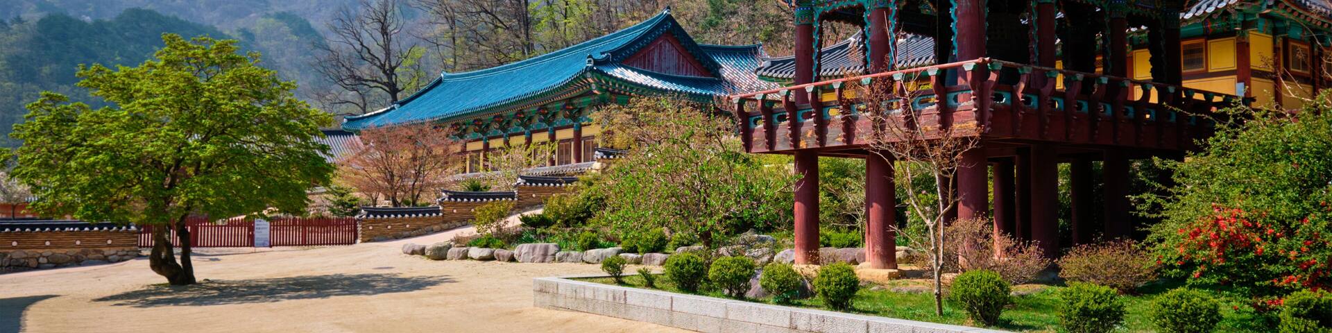 A traditional Korean palace with blue-tiled roofs, surrounded by a manicured garden and mountains in the background.