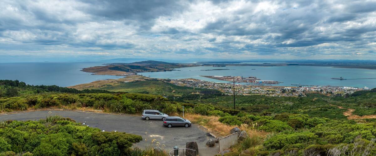 A coastal landscape with a road, vehicles, and a bridge over water.