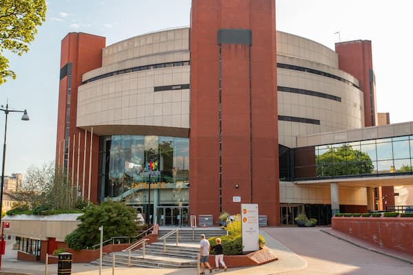 Um edifício moderno com fachada curva, grandes janelas de vidro e entrada destacada.