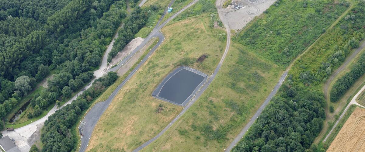 An aerial view of a rural area with a large open field, a pond, and a road network.