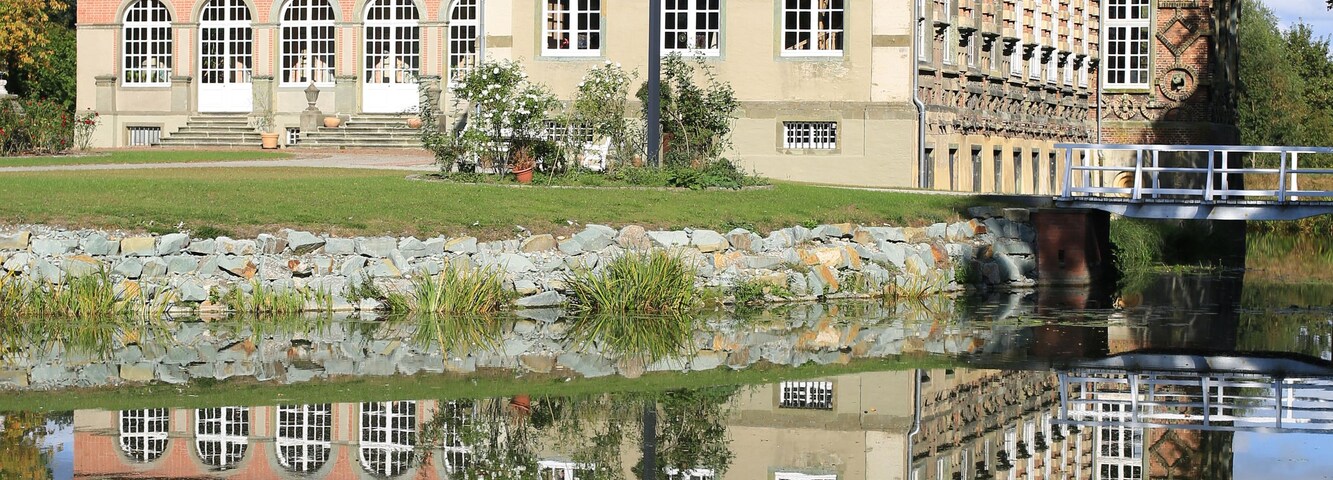 Un bâtiment historique doté d’une tour horlogée, d’un pont et d’une rivière paisible dans laquelle se reflète l’architecture.