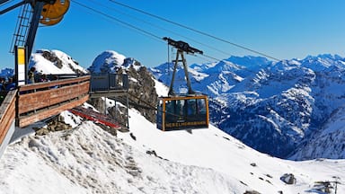 A cable car system with passengers, a wooden viewing platform, and snow-covered mountains in the background.