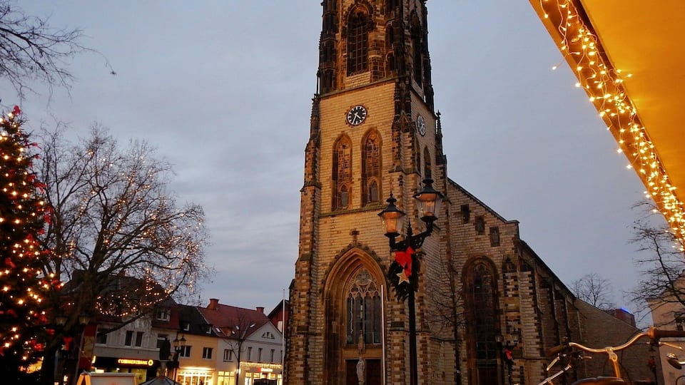 A historic church with a tall tower and clock, surrounded by buildings and festive lights.