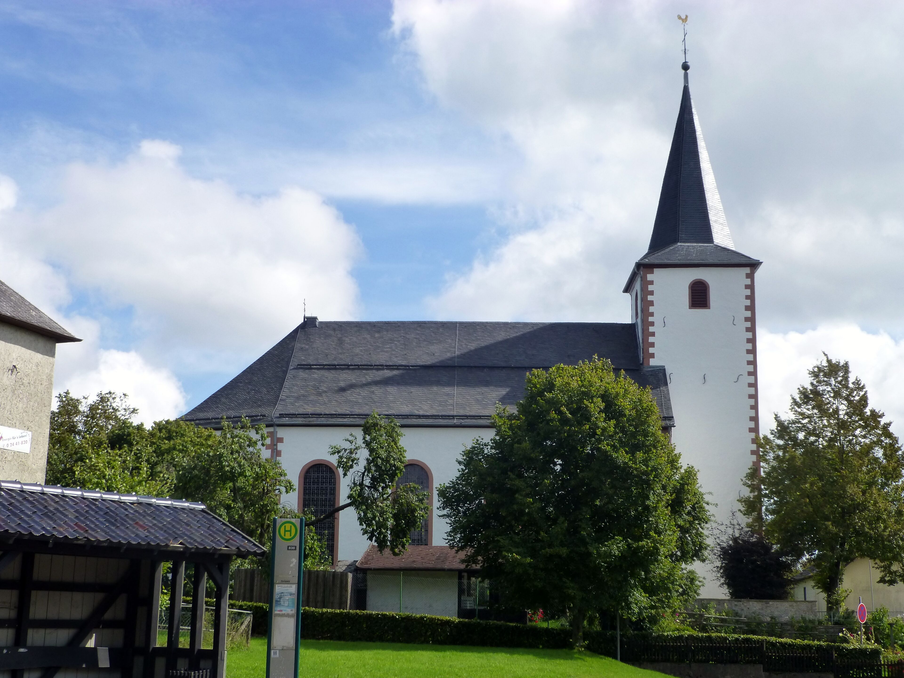 A church with a tall steeple and a clock tower, surrounded by trees and a well-maintained lawn.