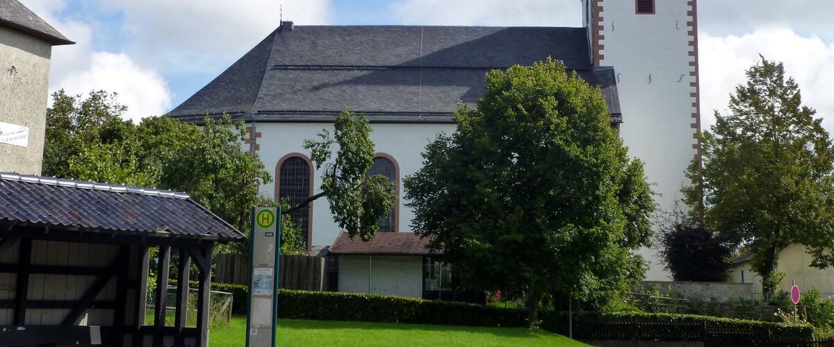 A church with a tall steeple and a clock tower, surrounded by trees and a well-maintained lawn.
