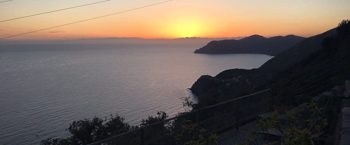 A sunset over a calm sea with rocky coastline and a wooden fence in the foreground.