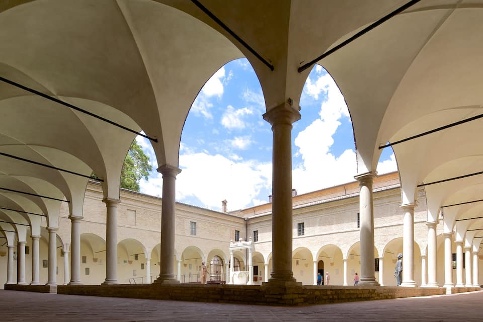 Un amplio patio con arcos y columnas, una estatua y un edificio al fondo.