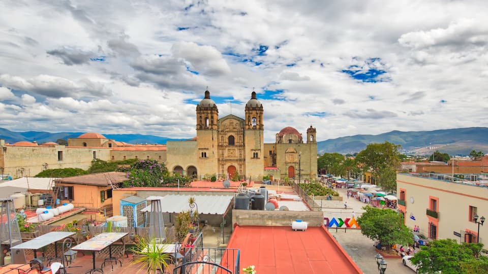 A historic cathedral with two towers, surrounded by urban buildings and a red-roofed plaza.