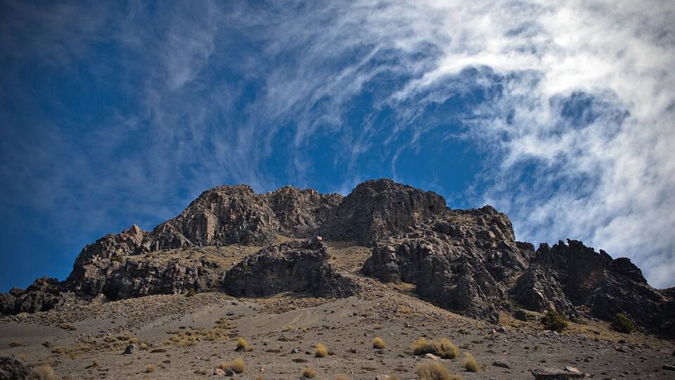 A rugged mountain range with sparse vegetation under a partly cloudy sky.