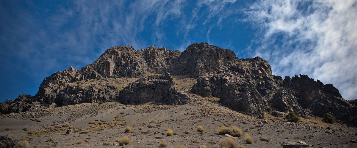 A rugged mountain range with sparse vegetation under a partly cloudy sky.