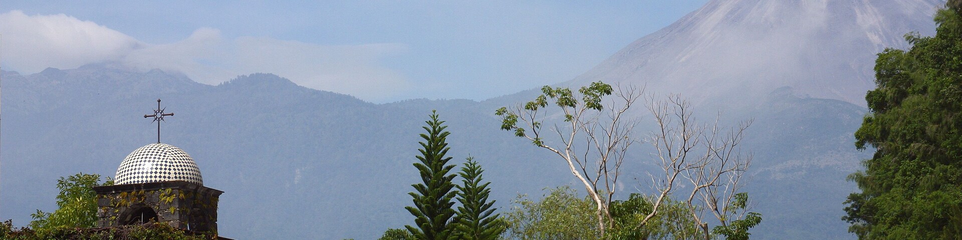 A mountain with a dome-shaped structure in the foreground and a volcano in the background.