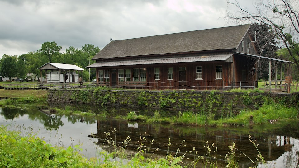 A rustic wooden building with a stone wall and a pond in front.