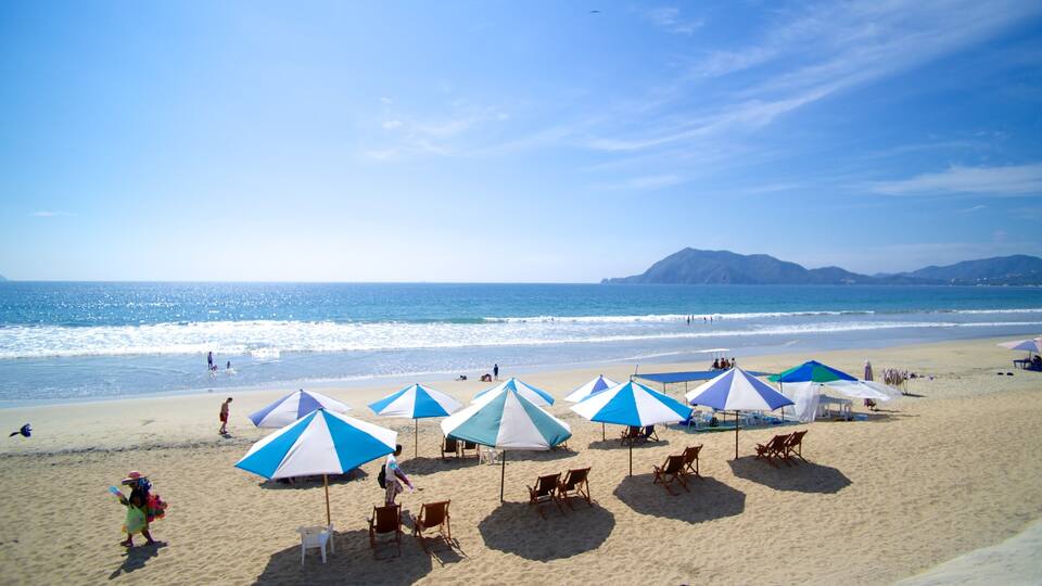 A beach with blue and white umbrellas, people, and a mountain in the background.