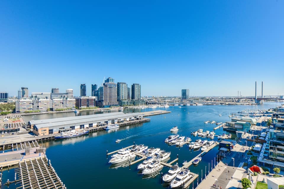 Un port de plaisance avec des bateaux amarrés, une vue sur les gratte-ciel de la ville en arrière-plan et un ciel bleu dégagé.