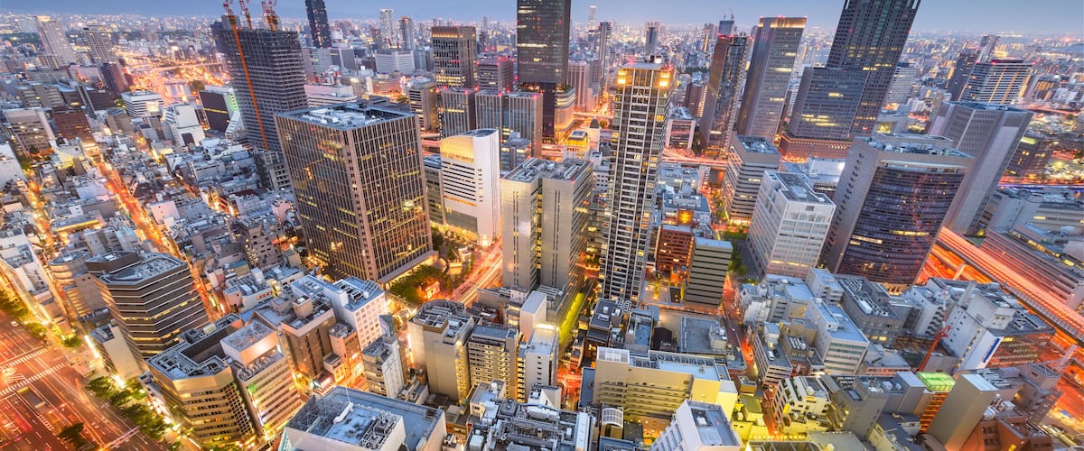 A cityscape at dusk with illuminated buildings and a busy street.