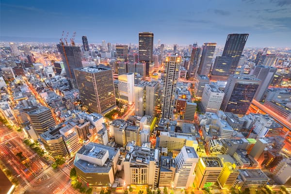 Paisagem urbana ao entardecer, com edifícios iluminados e rua movimentada.