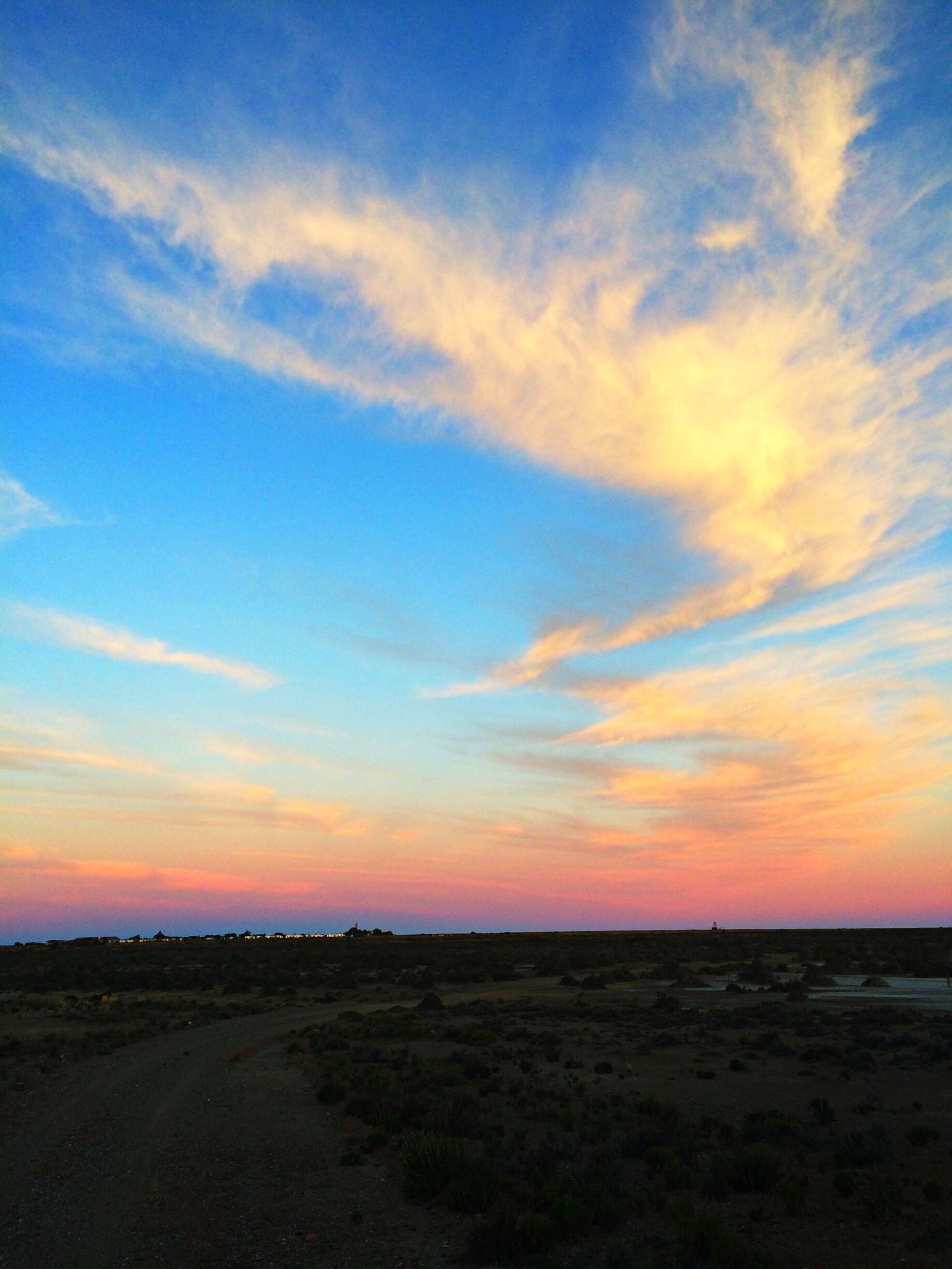 A sunset over a flat landscape with sparse vegetation and a distant structure.