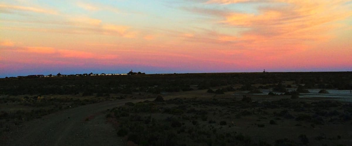 A sunset over a flat landscape with sparse vegetation and a distant structure.